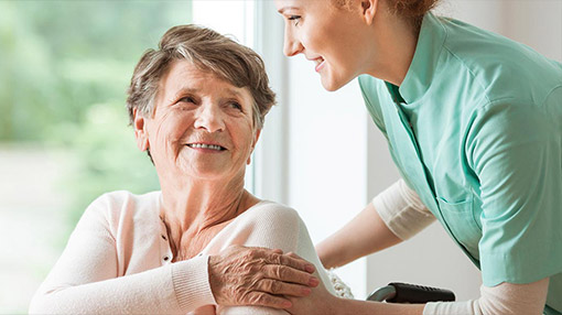 Seniorin im Rollstuhl lächelt zu Pflegerin auf