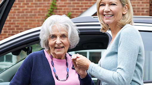 Dame hilft Seniorin beim Aussteigen aus dem Auto